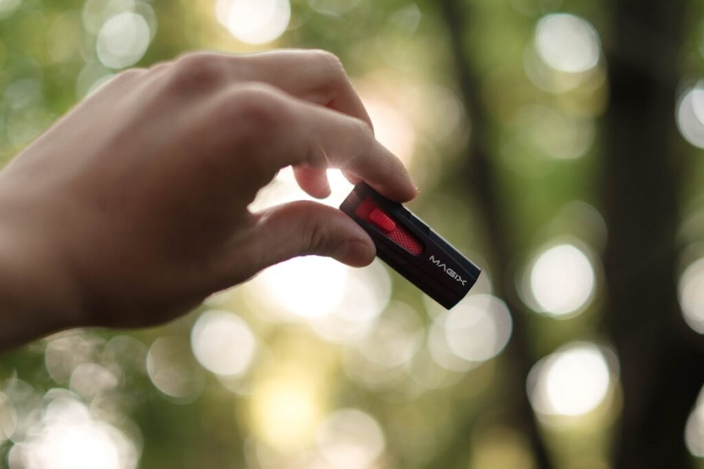 Close-up of a hand holding a USB drive outdoors with a bokeh background.