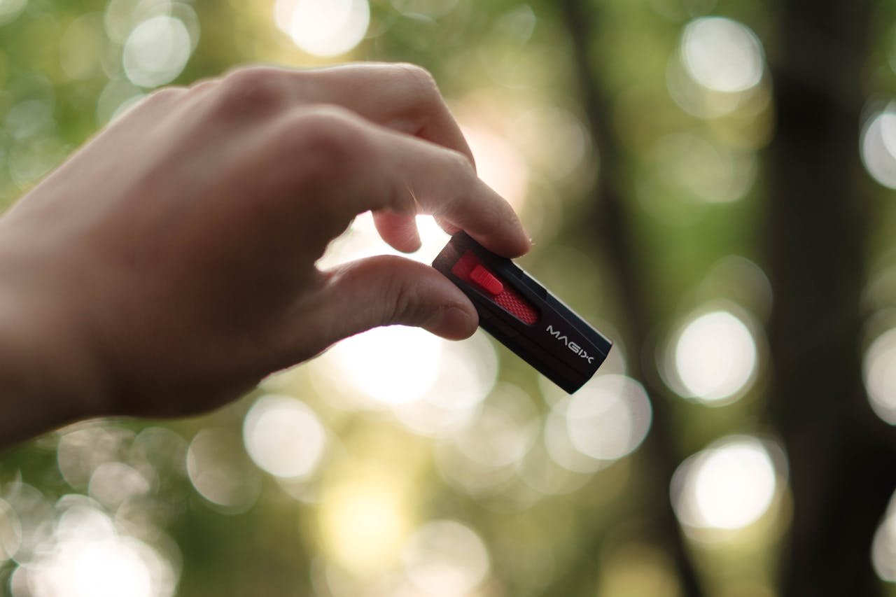 Close-up of a hand holding a USB drive outdoors with a bokeh background.